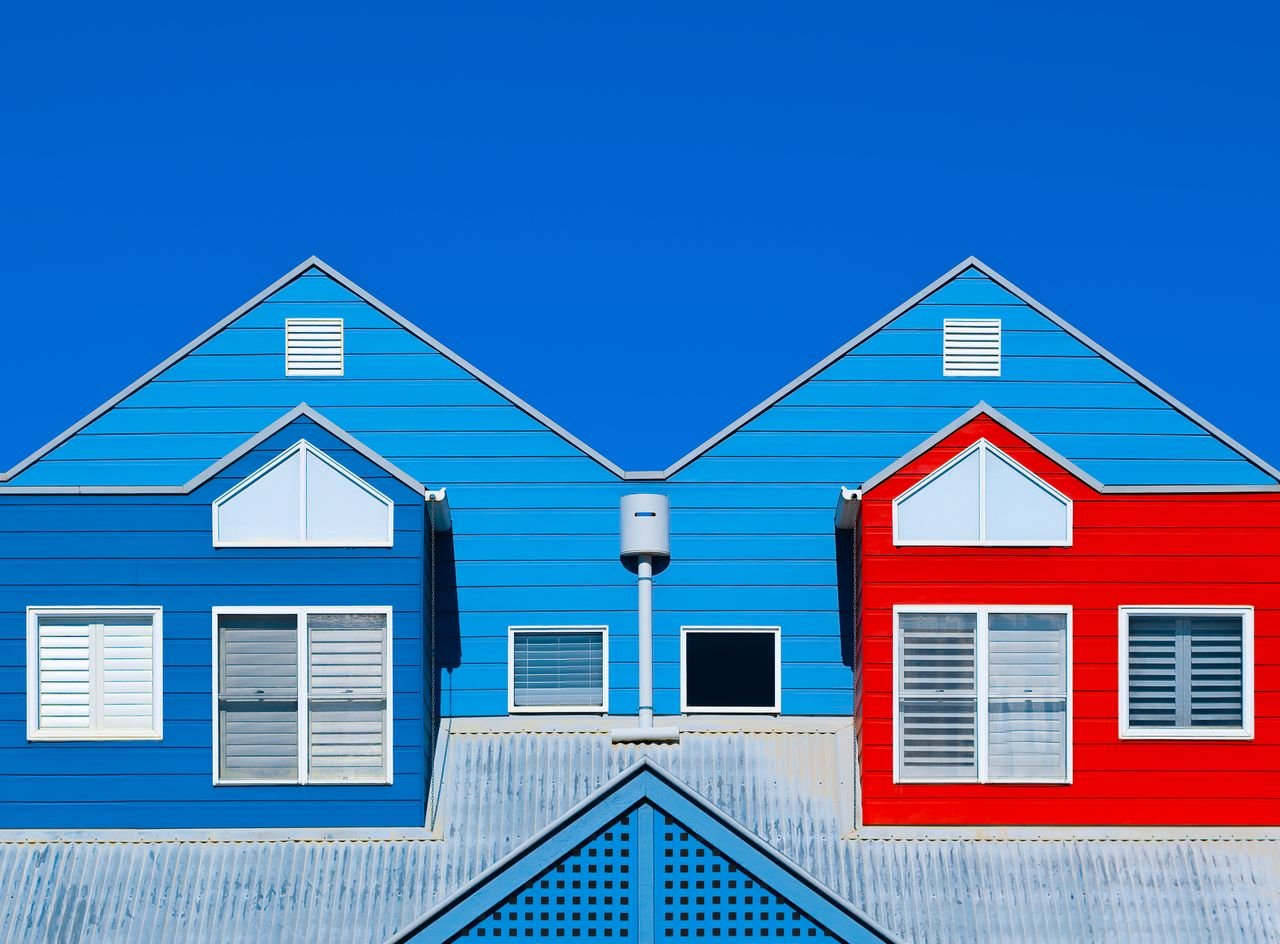 Mastering the First Impression: Your intriguing post title goes here Brightly painted house facades in blue and red create a striking contrast against a clear blue sky.