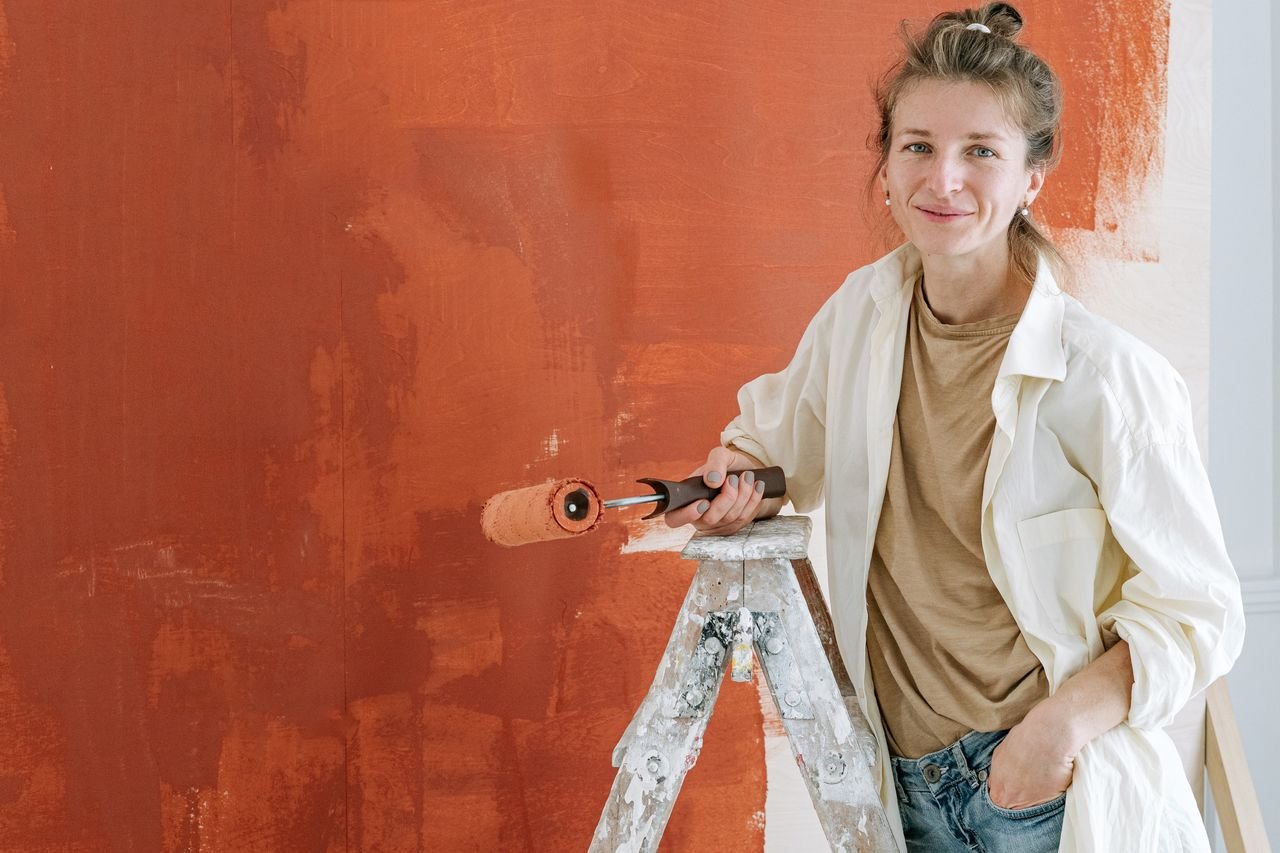 Woman smiling while painting a wall with a roller during a home renovation project.